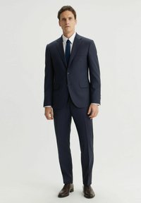 Granatowy garnitur o dopasowanym kroju, jednorzędowa marynarka, klapy w kształcie notcha i spodnie z gładkim przodem. W zestawieniu z ciemnobrązowymi butami eleganckimi.