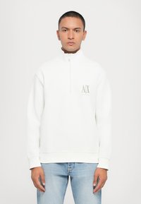 Vit sweatshirt med halv dragkedja, ribbade ärmslut och en logga i ljusgrått på bröstet. Har en avslappnad passform och mjuk textur.