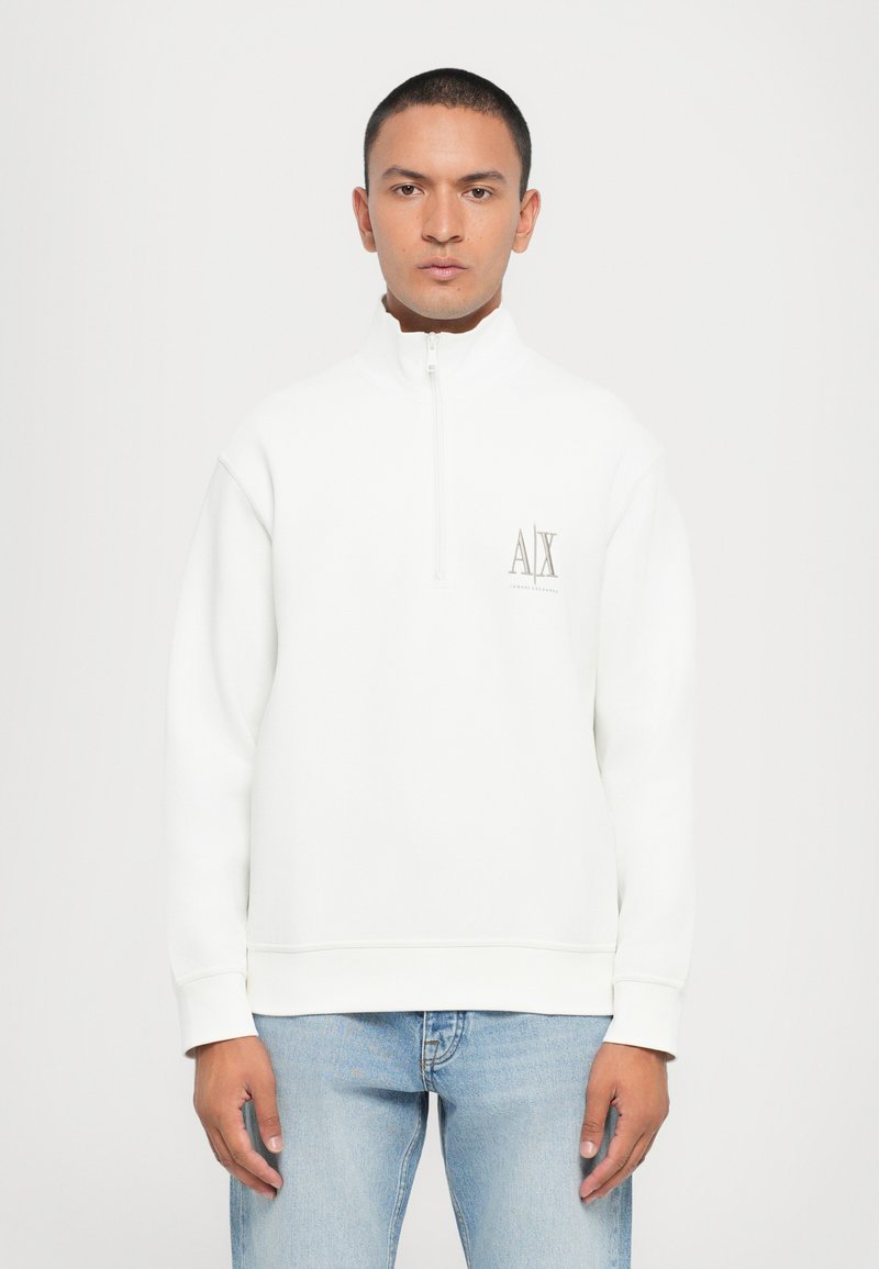 Vit sweatshirt med halv dragkedja, ribbade ärmslut och en logga i ljusgrått på bröstet. Har en avslappnad passform och mjuk textur.
