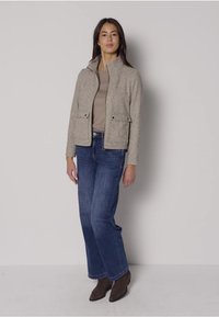 Grå tekstureret jakke med en tætsiddende krave, frontlommer og lynlåslukning; kombineret med blå flagrende jeans og brune ankelstøvler.