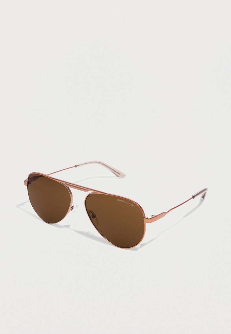 Γυαλιά ηλίου aviator με λεπτό μεταλλικό πλαίσιο σε ροζ χρυσό και καφέ φακούς τοποθετημένα σε λευκή επιφάνεια.