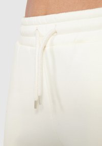 Pantalones de chándal blancos con cintura acanalada, que presentan un cordón con puntas metálicas y una tela suave y texturizada.
