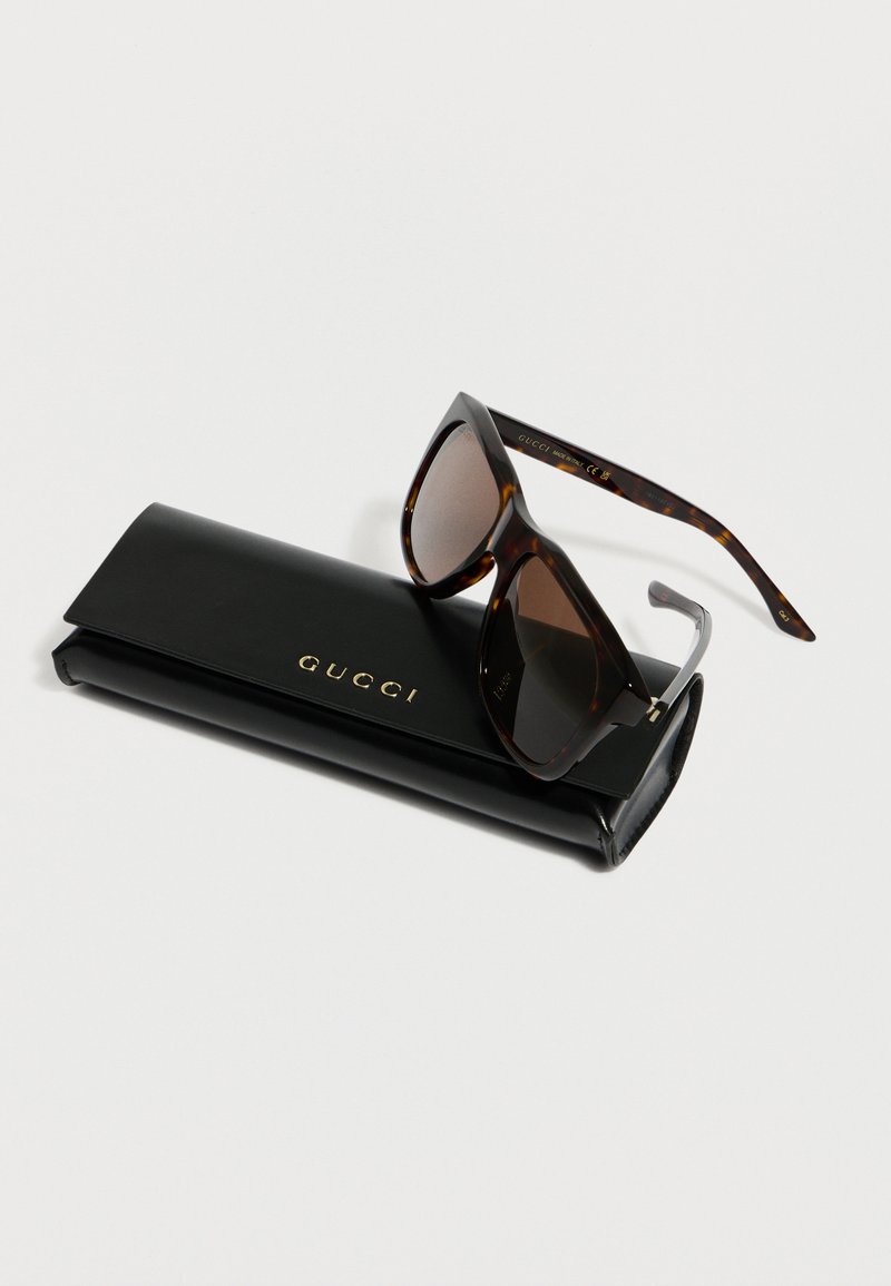 Tortoiseshell cat-eye sunglasses resting on a black leather Gucci case with gold logo lettering on a white surface.