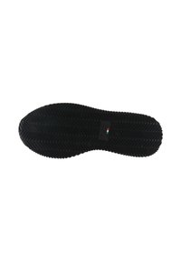 Suela de zapato con un patrón de tracción en zigzag negro y un pequeño logo de la bandera italiana cerca del centro sobre un fondo blanco.