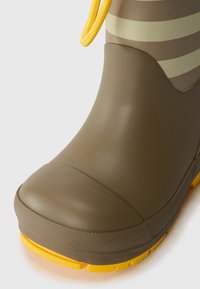 Bota de lluvia de goma verde con suela y acentos amarillos. Presenta una superficie texturizada y una punta redondeada, con un patrón de rayas cerca de la parte superior.