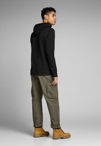 Black hoodie with a drawstring, green cargo pants with side pockets, and tan boots. The model is viewed from the back against a gray background.