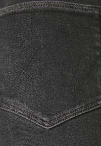 Tejido de mezclilla negro con una superficie texturizada, un bolsillo trasero con una solapa triangular y detalles de costura visibles.