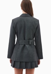 Blazer entallado de rayas gris oscuro con mangas largas, cinturón en la cintura y falda de capas. Tejido suave con un diseño estructurado.