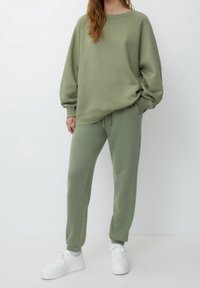 Lichtgroene sweatshirt met een ontspannen pasvorm en verlaagde schouders, gecombineerd met lichtgroene joggingsbroek, met elastische manchetten en een trekkoord in de taille. Witte sneakers.