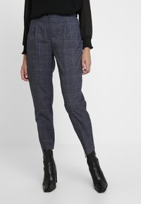 Grå rutiga byxor med skräddarsydd passform, med midja i normal höjd och sidfickor. Bärs med svarta klackstövlar.