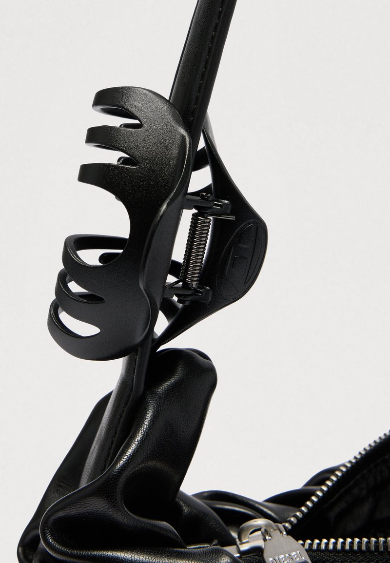 Black plastic hair claw clipped onto a black leather strap near a silver zipper pull on a bag.