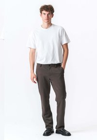 Brune bukser med slim fit, forsynet med knap- og lynlås-lukning, parret med en ensfarvet hvid t-shirt med korte ærmer og sorte sko.