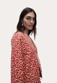 Rød mønstret kjole med blomstermotiv i creme, med dyb V-udskæring og lange ærmer. Letvægtsstof, afslappet pasform.