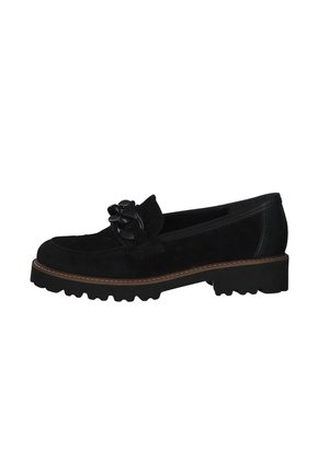 Mocassin en suède noir avec un détail de nœud décoratif sur le dessus. Caractéristiques une semelle épaisse et texturée avec un contour de couleur marron clair.