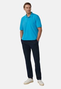 Polo turquoise avec col et manches courtes, associé à un pantalon marin et des baskets blanches. Tissu lisse et coupe décontractée.
