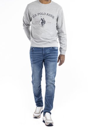 Šedá mikina s kulatým výstřihem a logem U.S. Polo Assn., v kombinaci s modrými džíny a šedými teniskami. Tento outfit má casual střih.