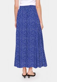 Modrá maxi sukně s bílým puntíkovaným vzorem, elastickým pasem, délka do poloviny lýtek a volný design. Texturovaná látka přidává objem.