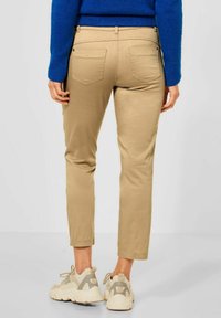Beige slim-fit broek, van katoen, vijf-pocket ontwerp met achterzakken, gecombineerd met chunky beige en grijze sneakers.