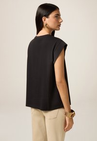 Top nero a maniche corte con vestibilità rilassata e scollatura rotonda, abbinato a pantaloni crema sartoriali. Visibile un bracciale elegante in oro.