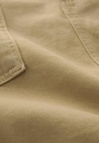 Close-up beežist kangast, millel on nähtav diagonaalne twill-kude ja õmmeldud õmblusdetail rõivaste materjalis.