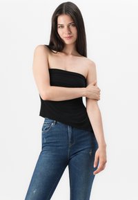 Svart strapless topp i mjukt tyg, med en åtsittande design. Matchad med medelblå denimjeans, slät textur och klassisk snitt.