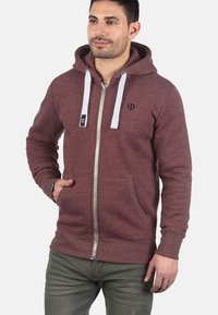 Maroon zip-up hoodie made of soft fabric, featuring a white drawstring, two front pockets, and a small logo on the chest.