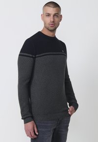 Suéter de punto en azul marino y gris oscuro con un patrón texturizado, cuello redondo, mangas largas y puños ajustados. Presenta un detalle de rayas horizontales.