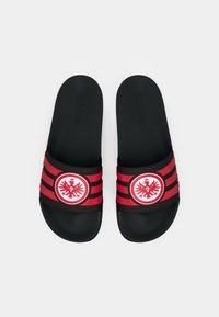 Μαύρα σανδάλια τύπου slide με κόκκινη και μαύρη ριγέ ταινία. Διαθέτουν κυκλικό λογότυπο στο κέντρο με σχέδιο αετού. Υπόδημα με υφή για καλύτερο κράτημα.