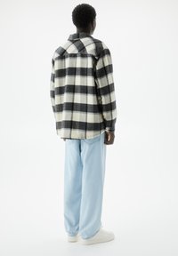 Koszula flanelowa w czarno-białą kratę, o luźnym kroju i długich rękawach. Nosi się ją z jasnoniebieskimi dżinsami i białymi tenisówkami. Widok z tyłu.