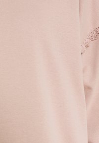 Maglione rosa chiaro con una texture morbida e liscia. Presenta un bordo in pizzo su una manica, che aggiunge un tocco delicato al design.
