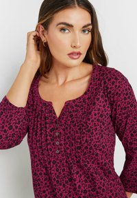 Top fucsia con motivo floreale nero, scollatura a V, chiusura con bottoni e maniche a tre quarti; tessuto morbido con dettagli arricciati.