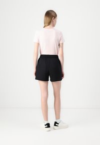 Pink short-sleeve t-shirt and black athletic shorts with an elastic waistband, paired with white sneakers featuring black accents.