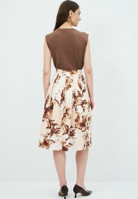 Top marrone senza maniche, gonna a fiori beige con accenti marroni, design plissettato, abbinata a tacchi neri a punta.