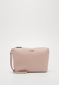 Pochette en cuir rose pâle avec une finition texturée, logo doré à l'avant, fermeture éclair et bandoulière amovible.