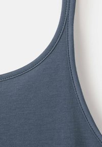 Gros plan sur la bretelle et l'encolure d'un débardeur en tissu bleu, montrant des doubles surpiqûres sur un matériau lisse et doux.