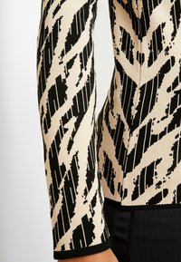 Maglione a maglia a strisce nero e crema con un design testurizzato, maniche lunghe e orlo a coste nero.
