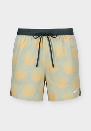 Svetlo zelené bežecké šortky Nike s veľkými vyblednutými oranžovými kruhovými vzormi, čiernym šnúrkovým pásom a bielym logom Nike Swoosh na ľavej nohe.