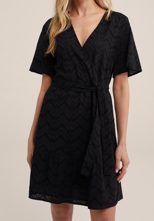 Schwarzes Wickelkleid mit kurzen Ärmeln, das ein Zickzackmuster, einen tiefen V-Ausschnitt und einen Taillengürtel aufweist. Der Stoff hat ein strukturiertes, gemustertes Design.