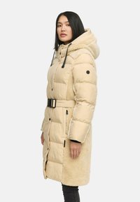 Beige pufferjas met een pluizige, sherpa-structuur aan de zijkant, verstelbare capuchon, riemdetail en knoopsluiting, met een rechte pasvorm.