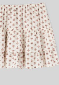 Jupe blanche à volants présentant de petits motifs floraux rouges, taille élastique et tissu léger à texture.