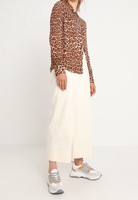 Camicia a maniche lunghe con stampa leopardata e chiusura con bottoni, pantaloni larghi crema e sneaker grigie chunky con dettagli arancioni e gialli.
