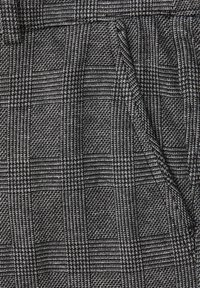 Tissu tissé gris avec un motif à carreaux texturé comportant des carrés alternés et des plis structurés. Les accents comprennent un design de poche élégant.