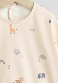 Tessuto color pesca con illustrazioni di animali, tra cui una giraffa, un leone e un elefante. Presenta un collo rotondo e una texture liscia.