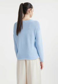 Maglione azzurro chiaro a coste, con maniche lunghe e vestibilità rilassata, caratterizzato da un collo rotondo e una superficie liscia. Indossato con pantaloni color crema.