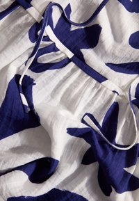 Witte stof met grote marineblauwe bloemenpatronen, gestructureerd en gedrapeerd om plooien te tonen met een smalle strikdetail langs de rand.