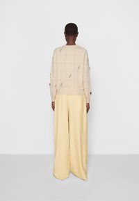 Beżowy sweter dziany z wzorem liści, w oversize'owym kroju, z długimi rękawami. Połączony z luźnymi, jasnoszarymi spodniami. Gładka tekstura.