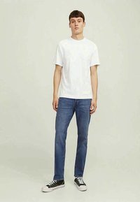 Tricou alb din bumbac cu mâneci scurte, asortat cu blugi albaștri din denim și adidași negri cu șireturi albe și design cu glezna joasă.