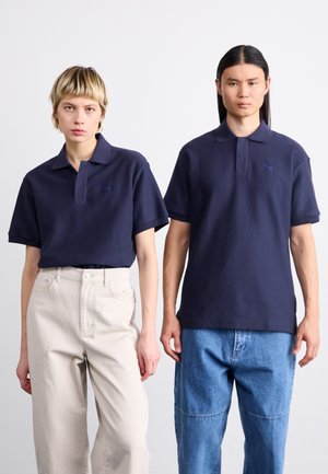 Tricouri polo de culoare bleumarin, cu un țesătură texturată; prezentând mâneci scurte și un guler. Cămașa din stânga are un mic logo, asortată cu pantaloni bej deschis.