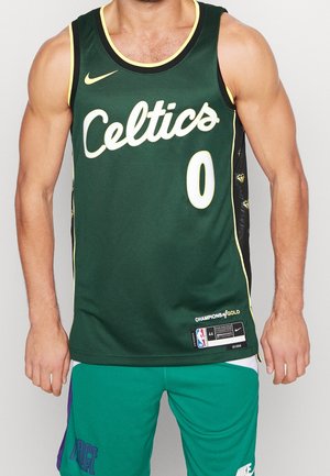 Mężczyzna w zielonym koszulce do koszykówki Boston Celtics z numerem 0 oraz dopasowanych zielonych szortach sportowych, stojący na jednolitym tle.