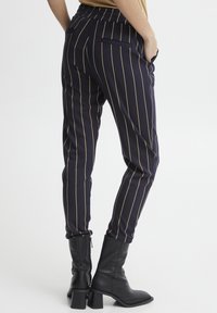 Marinrandiga byxor med guldfärgade vertikala linjer, elastisk midja, sidofickor, tapered fit och tillsammans med svarta blockklackstövlar.